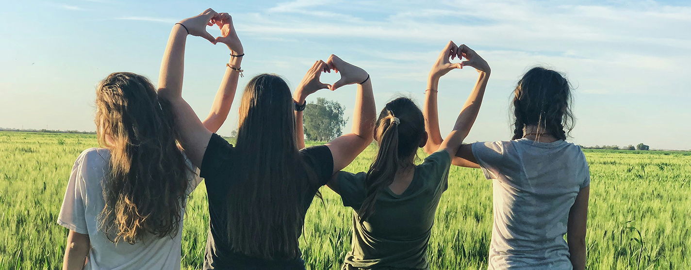 field of green grass with friends linking arms and making hearts with each other's hands