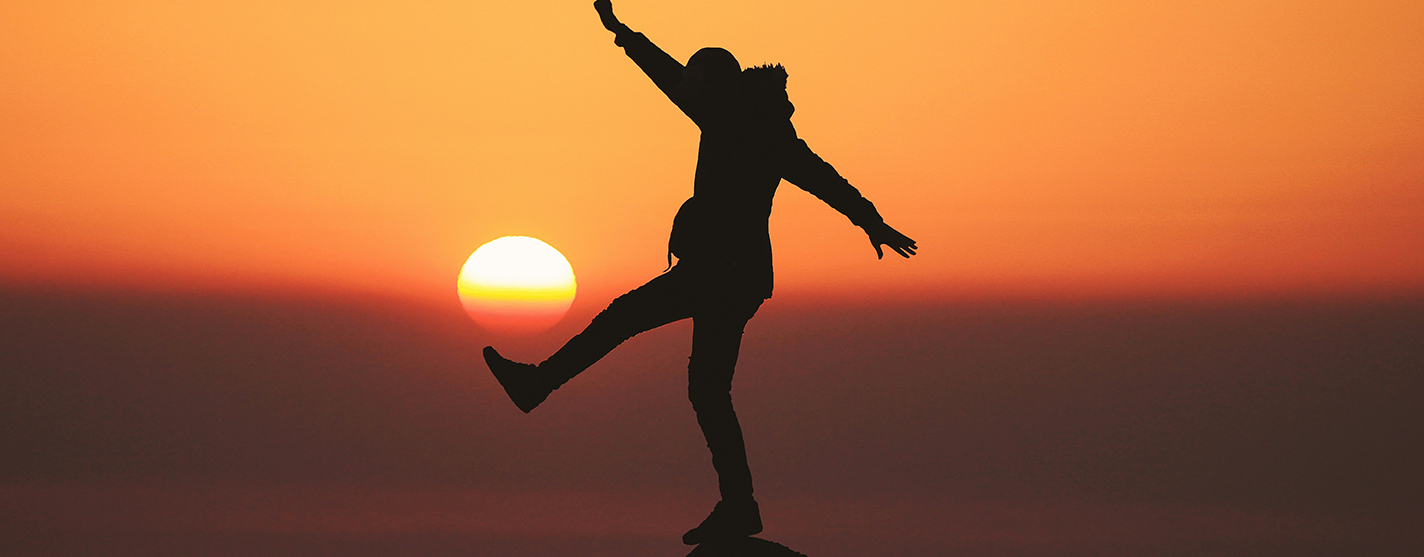 image of a woman balancing on a rock by the ocean at sunset