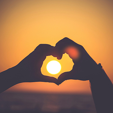 sunset with two people's hands forming a heart around the sun